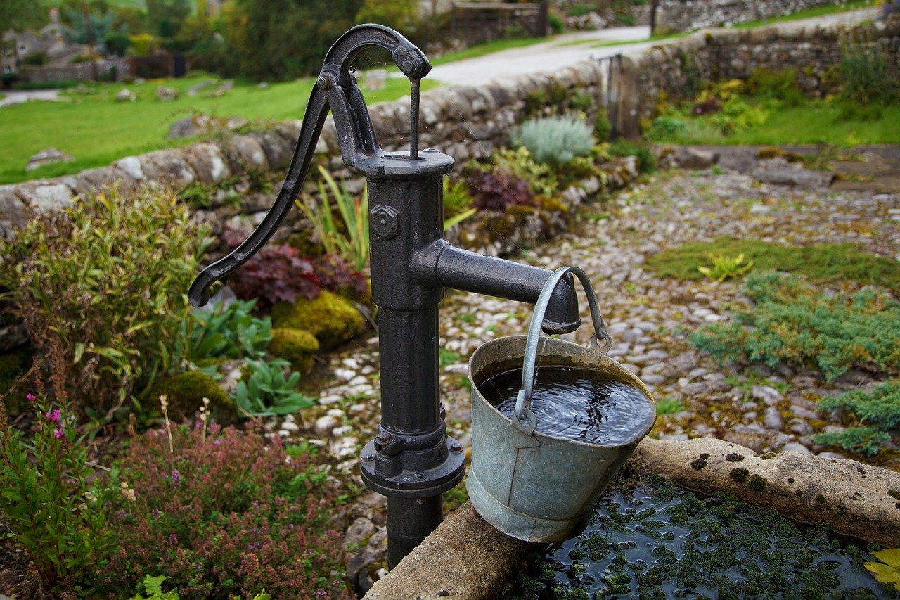 Alte wasserpumpe an einem brunnen im garten bewässerung und einsparung von  wasser ländliche umgebung